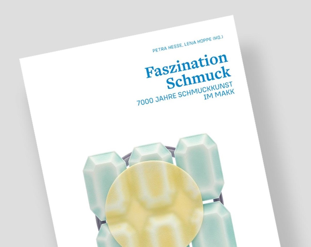 Das angeschnittene Cover eines Magazins auf grauem Hintergrund: auf dem Titel in blauer Schrift der Titel der Ausstellung und ein Schmuckobjekt.