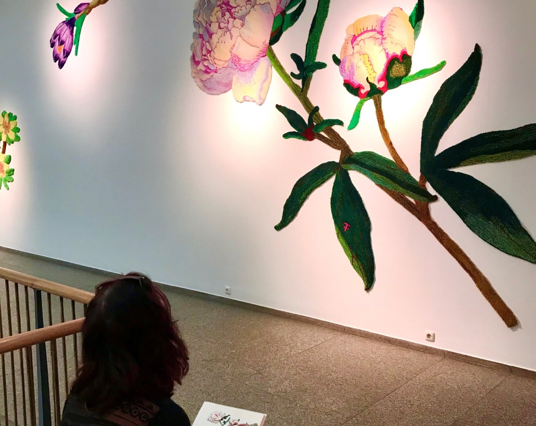 A woman sits on the bottom step of a staircase in the MAKK and looks at a painting of a flower directly on the wall in front of her.