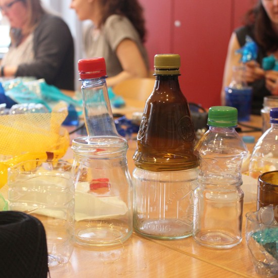 Frauen sitzen an einem Tisch und basteln mit zerschnittenen Plastikflaschen.