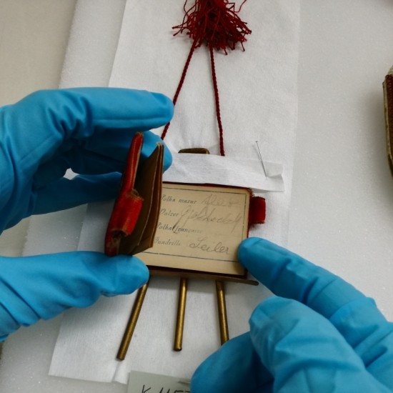 Eine Nahaufnahme von zwei Händen in blauen Gummihandschuhen, die ganz vorsichtig ein historisches Ausstellungsstück berühren.