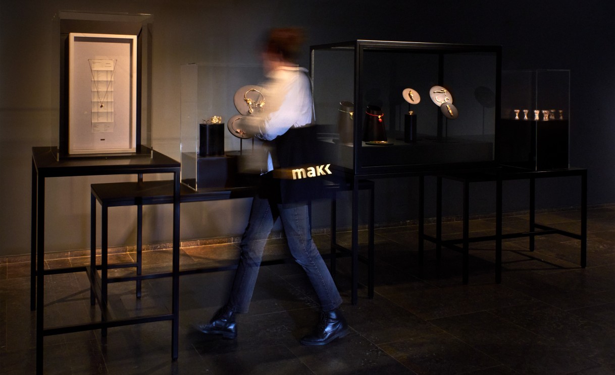 Eine Frau mit weißer Jacke und schwarzer Tasche geht durch die Schmuckausstellung.