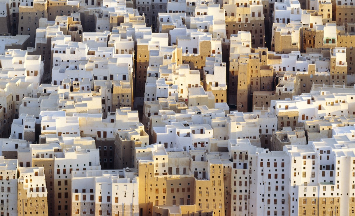 Aufsicht auf die historische Stadt Shibam mit hochen, schmalen Häusern in Weiß und Ocker.