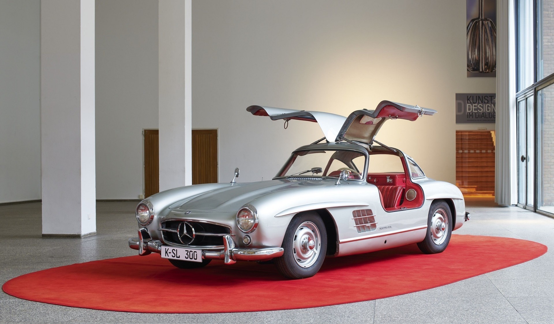 A silver vintage car with upward-opening gullwing doors on a red carpet.