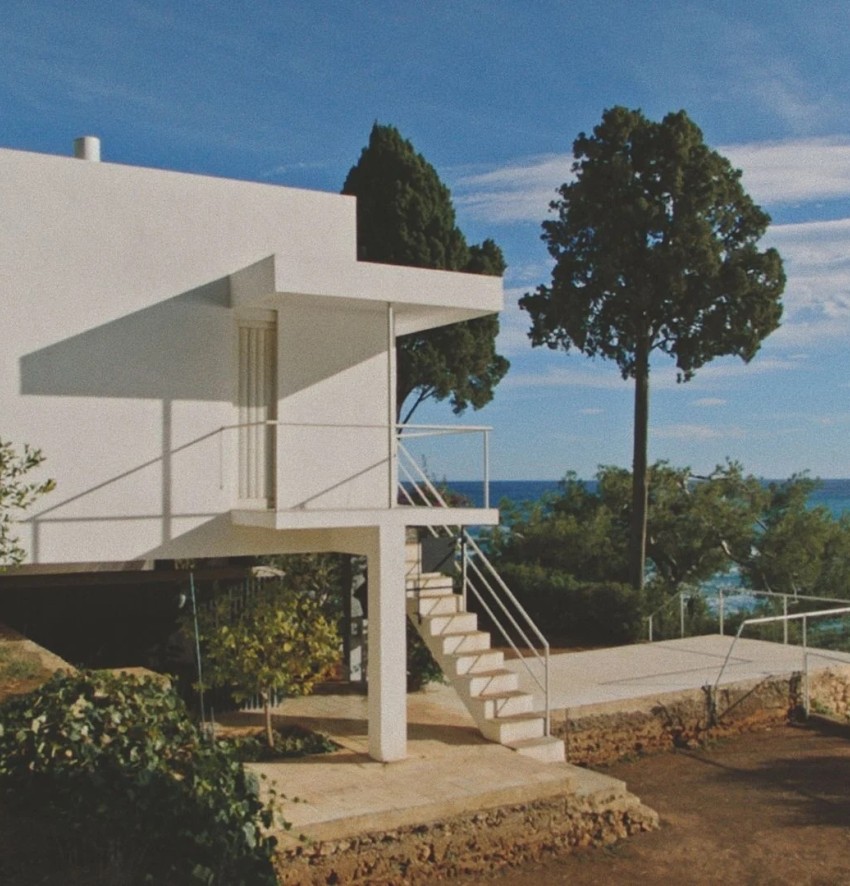 Weißer Bungalow mit freier Treppe und Blick aufs Meer.