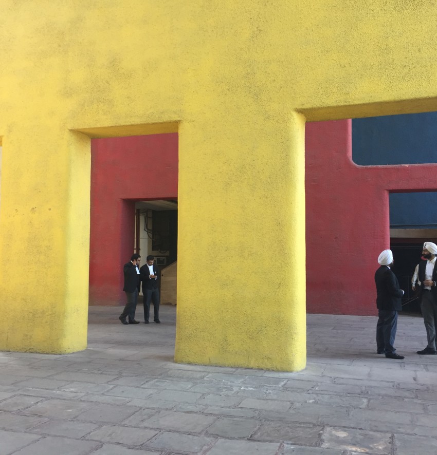 Gebäude mit modernem Säulengang, gelb getüncht. Dazwischen vier Männer.