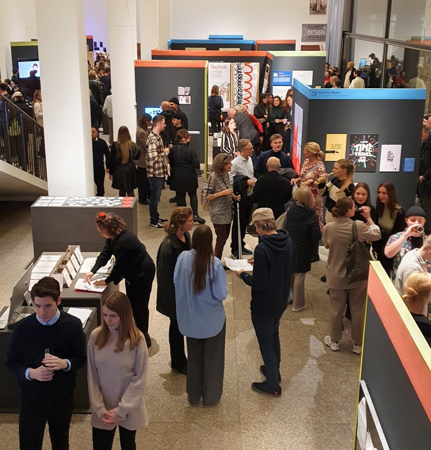 A view into an exhibition room at the MAKK, small groups of people looking at exhibition objects or talking to each other.