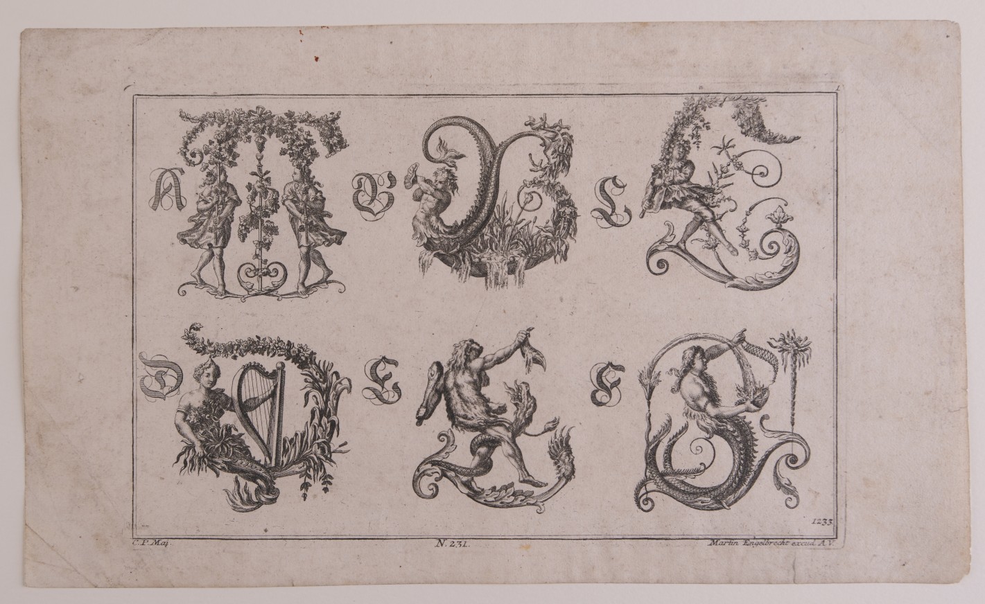 Buchstaben aus figürlichen Elementen zusammengesetzt, wie Menschen, Tieren und Mischwesen, sowie Fruchtbündeln, Blumengirlanden und Ranken.