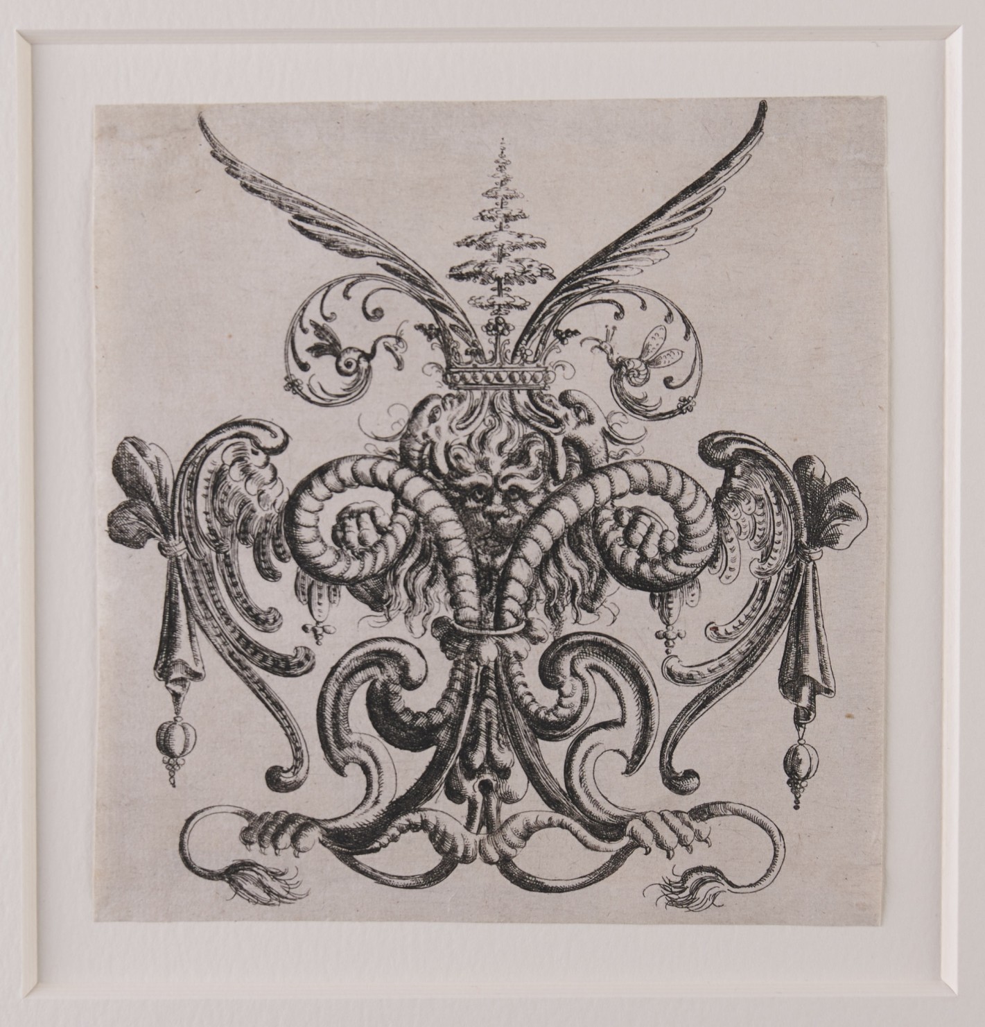 Fantasievolles Zierornament mit mittiger Löwenfratze. Pranken des Löwen liegen auf den symmetrischen Schnörkeln oder wachsen aus ihnen heraus. Über dem Tier ist ein Baum angedeutet.